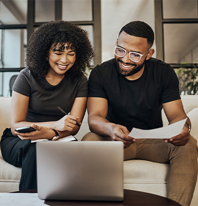 Two people sitting in front of laptop holding papers and cell phone