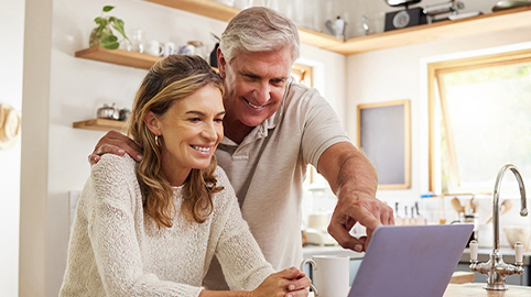 Couple in kitchen reading and pointing on laptop