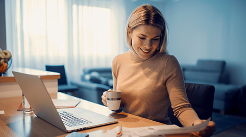 Woman happily looking through financial papers in front of a computer